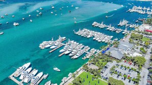 An aerial view of a marina with numerous boats docked, a bridge in the background, and a parking area with cars and greenery. - Beach Condo | Hot Tub | Kitchen | Pet-Friendly (West Palm Beach)