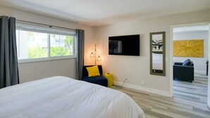 A hotel room with a large bed, a TV mounted on the wall, a sofa with yellow cushions, and a large mirror. - Beach Condo | Hot Tub | Kitchen | Pet-Friendly (West Palm Beach)
