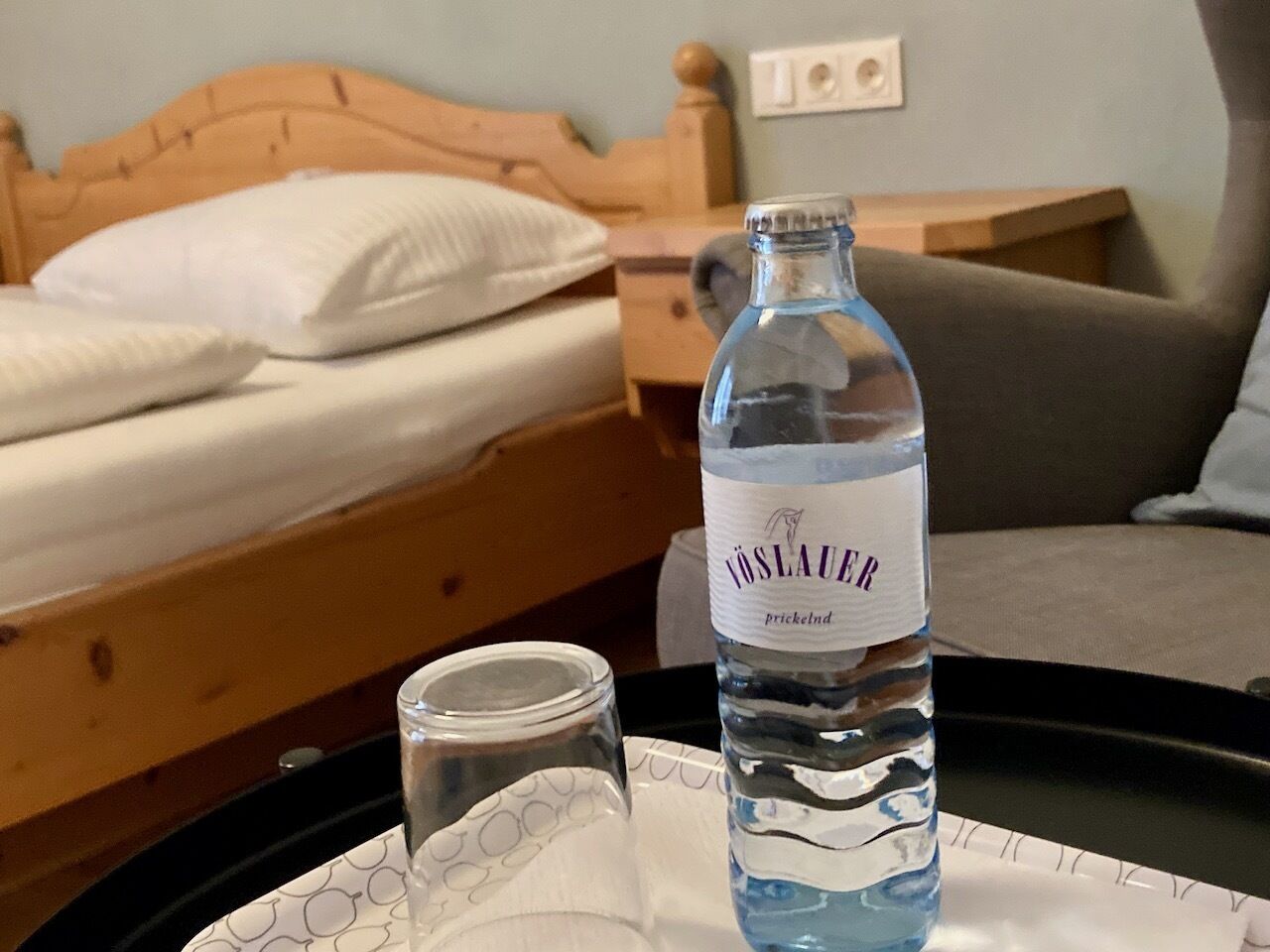 A bed with white pillows, a wooden headboard, and a nightstand with a bottle of water and a glass.