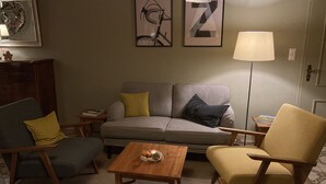 Una sala de estar con un sofá, dos sillones, una mesa de centro y una lámpara. En la pared hay cuadros enmarcados.