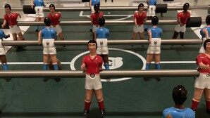 Un juego de mesa con miniaturas con uniformes rojo y azul, dispuestas sobre un campo de juego verde con líneas blancas.