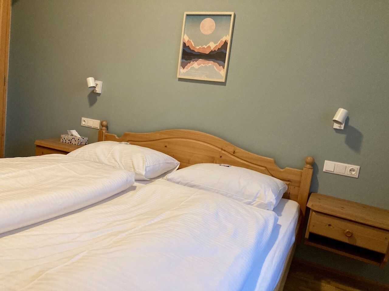 Uma cama de casal com roupa de cama branca, cabeceira de madeira e mesa de cabeceira com abajur.
