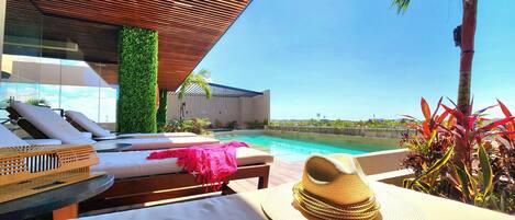 A poolside lounge area with sun loungers, a pool, and a view of the city skyline.