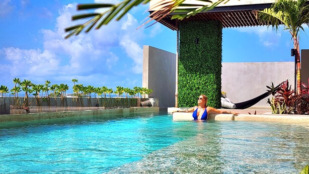 Un área de piscina con agua cristalina, una hamaca y palmeras.