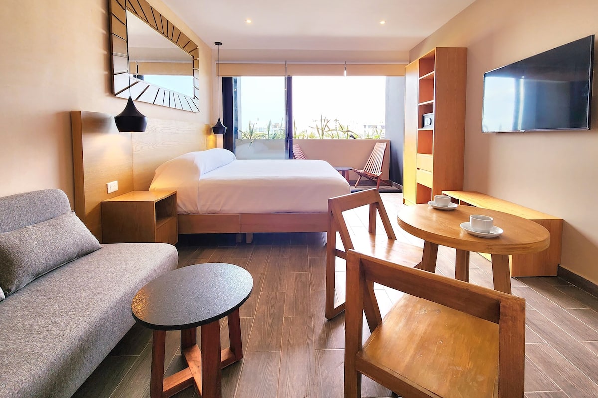 Een hotelkamer met een bed, een slaapbank, een klein rond tafeltje, een televisie en een boekenkast.