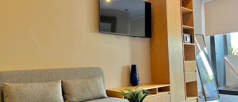 Una sala de estar moderna con un sofá gris, un televisor montado en la pared, un mueble de madera y una planta en una mesa redonda.