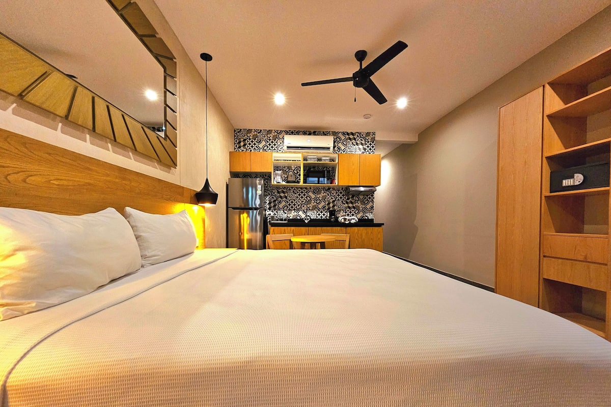 Een moderne hotelkamer met een groot bed, een kleine kitchenette, een plafondventilator en houten planken.