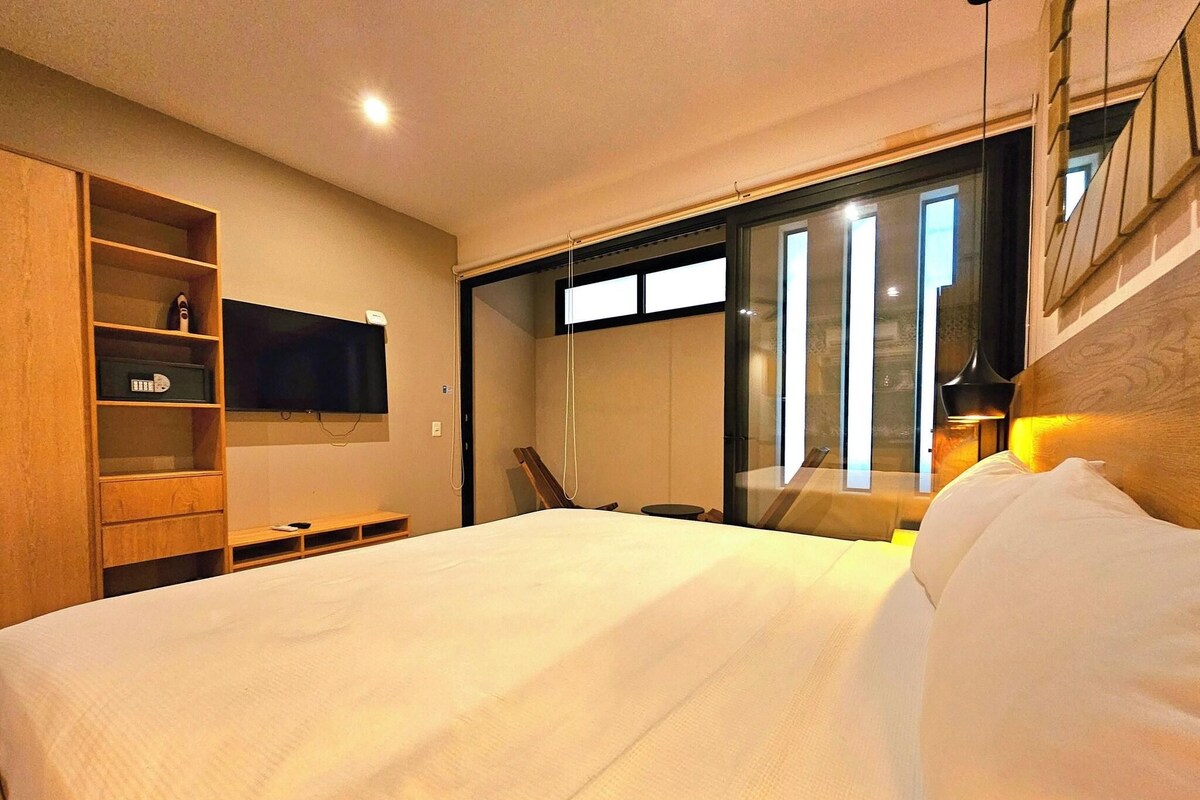 Een moderne hotelkamer met een groot bed, een aan de muur bevestigde televisie, een houten garderobe en een glazen schuindeur naar een balkon.