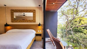Un dormitorio moderno con una cama grande, cabecera de madera, ventilador de techo y vista a árboles a través de una puerta de vidrio.