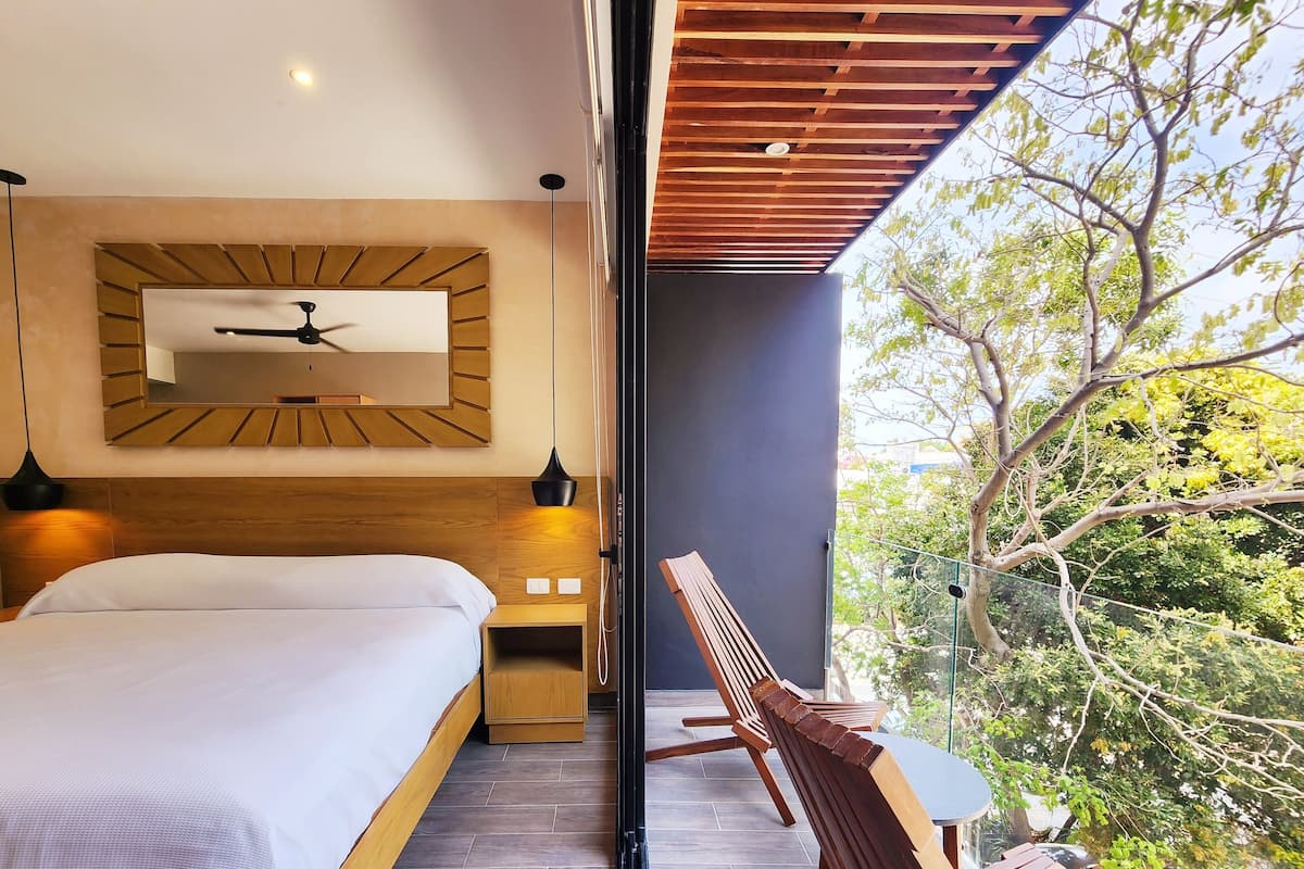 Een moderne slaapkamer met een groot bed, een houten hoofdbord, een plafondventilator en uitzicht op bomen door een glazen deur.