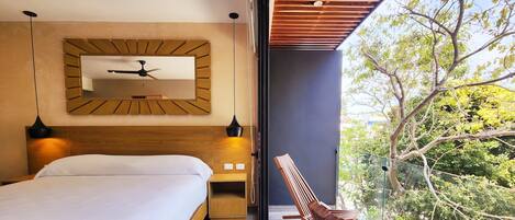 A modern bedroom with a large bed, a wooden headboard, a ceiling fan, and a view of trees through a glass door.
