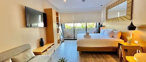 Ett modernt hotellrum med en säng, soffa, TV, takfläkt och utsikt över grönområden utanför.