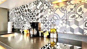 Una cocina con salpicadero blanco y negro a cuadros, una cafetera y varios utensilios de cocina sobre la encimera.