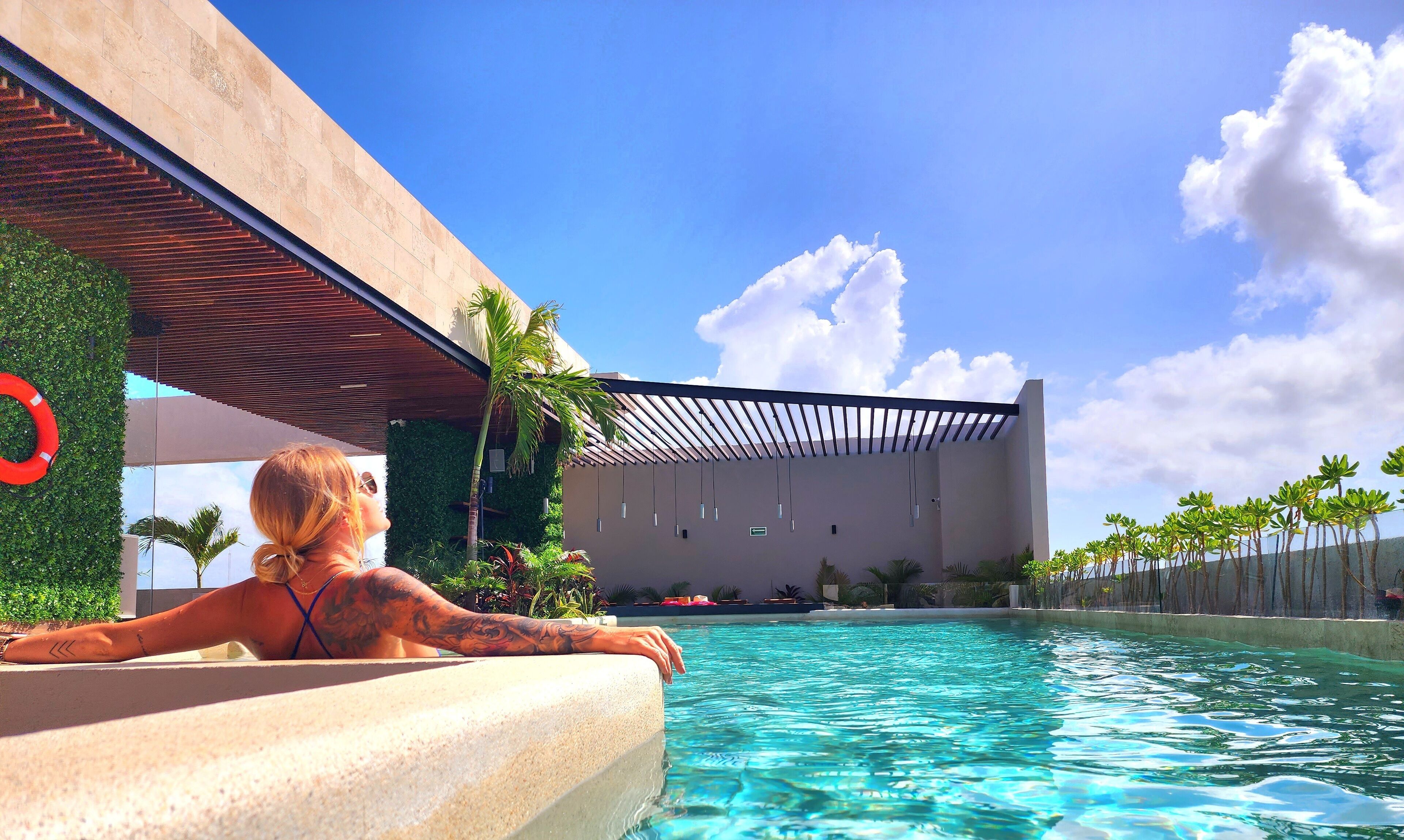 Vista de la piscina con un edificio moderno, un flotador salvavidas y plantas tropicales.