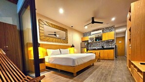 Una habitación de hotel moderna con una cama grande, muebles de madera, una kitchenette y un ventilador de techo.
