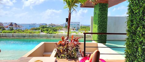 A poolside lounge with a view of the ocean, a palm tree, and a green vertical garden.