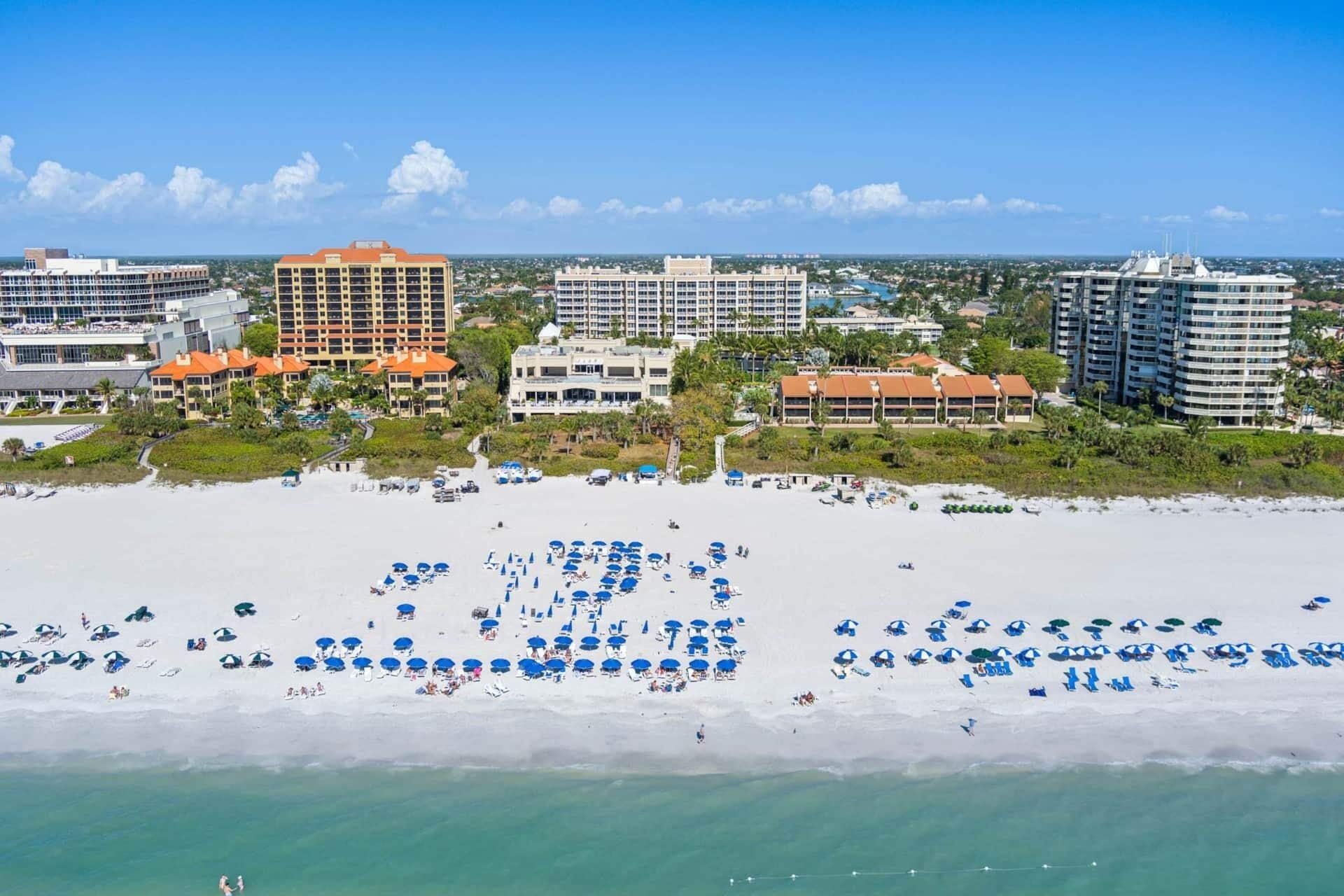 Una playa con numerosos sombrillas y tumbonas, rodeada de hoteles y edificios.