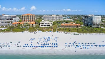 Una playa con numerosos sombrillas y tumbonas, rodeada de hoteles y edificios.
