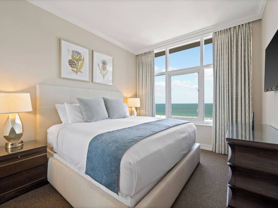 A hotel room with a large bed, two bedside tables with lamps, a flat-screen TV, and a window with curtains.