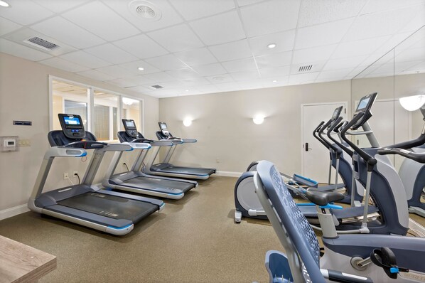 A gym with multiple treadmills and elliptical machines, carpeted floor, and a door leading to another room.