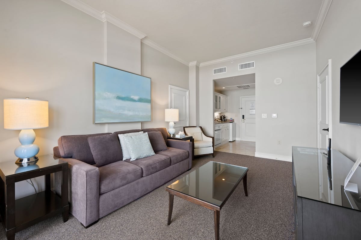 A modern living room with a grey sofa, a glass coffee table, and a TV on a cabinet.