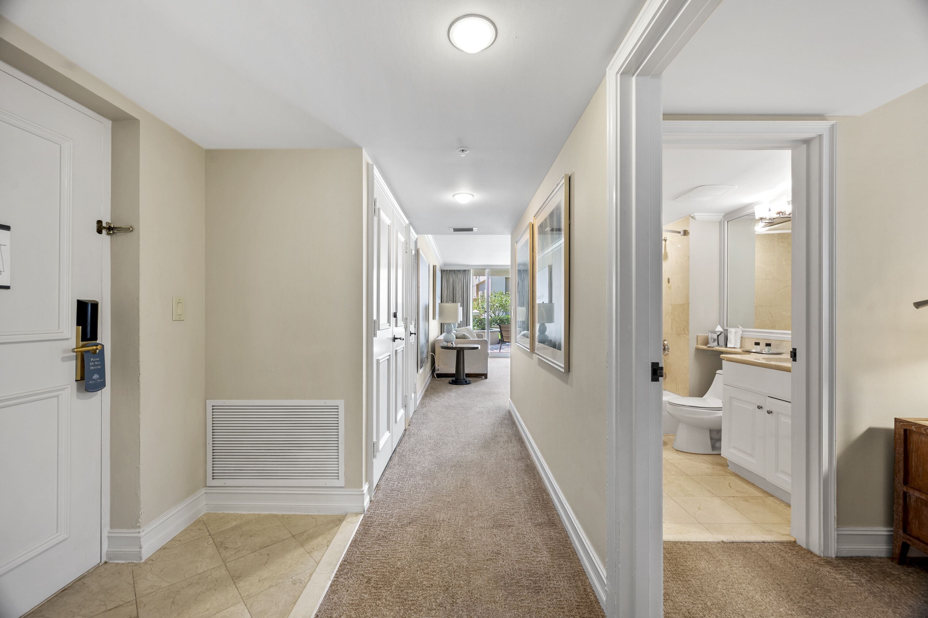 A hallway with a carpeted floor, white walls, and a door on the left.