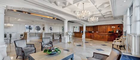 A spacious lobby with a high ceiling, chandeliers, and a reception area.