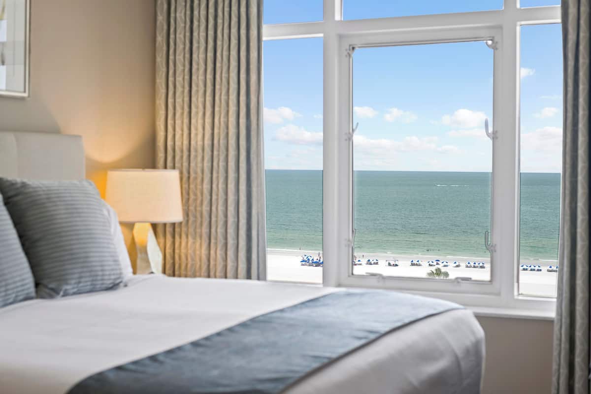A hotel room with a large window offering a view of the beach and ocean.