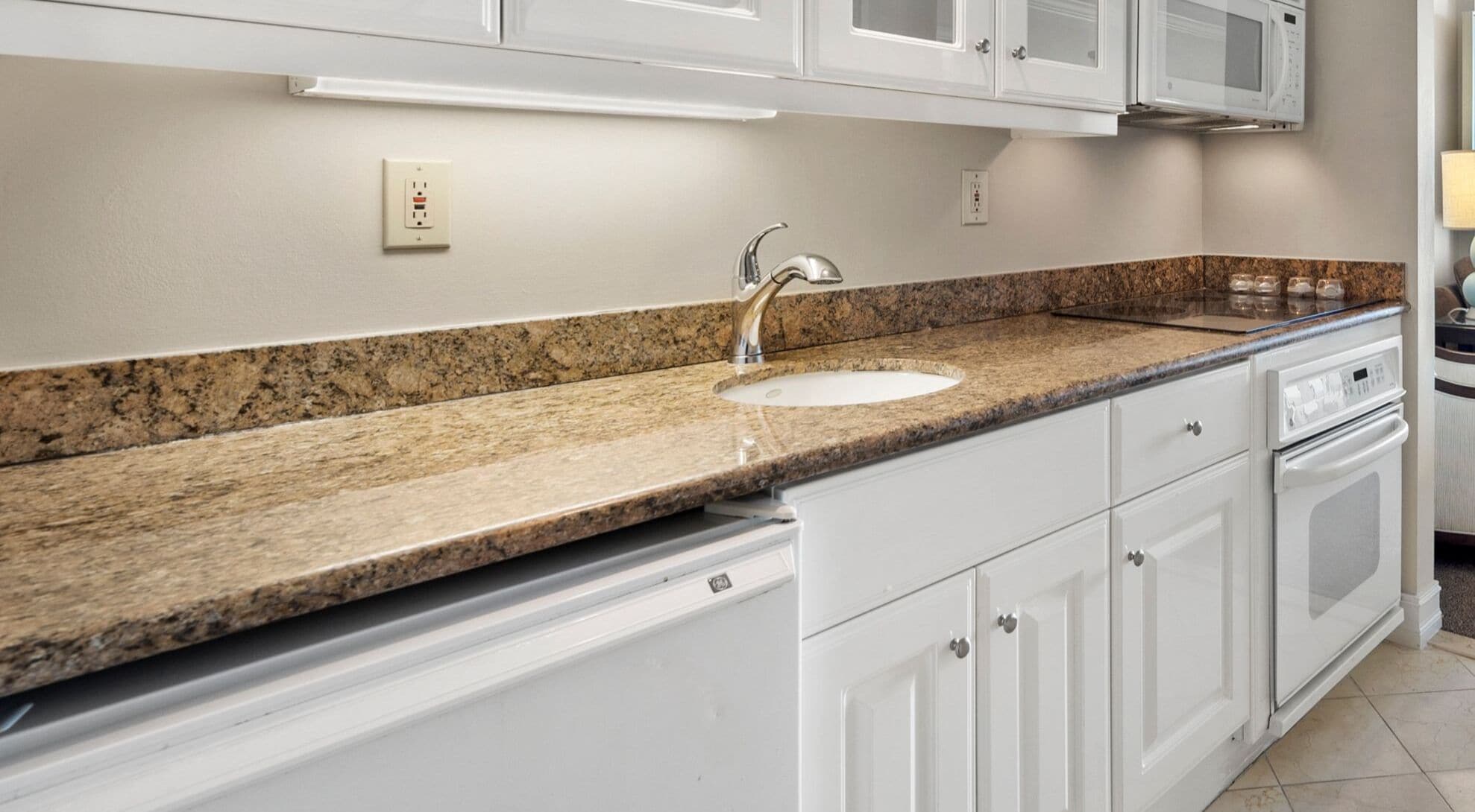 A kitchen with white cabinets, a granite countertop, a stainless steel sink, and a built-in oven.
