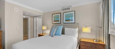 A hotel room with a large bed, two bedside tables, a nightstand, a lamp, and two framed pictures on the wall.