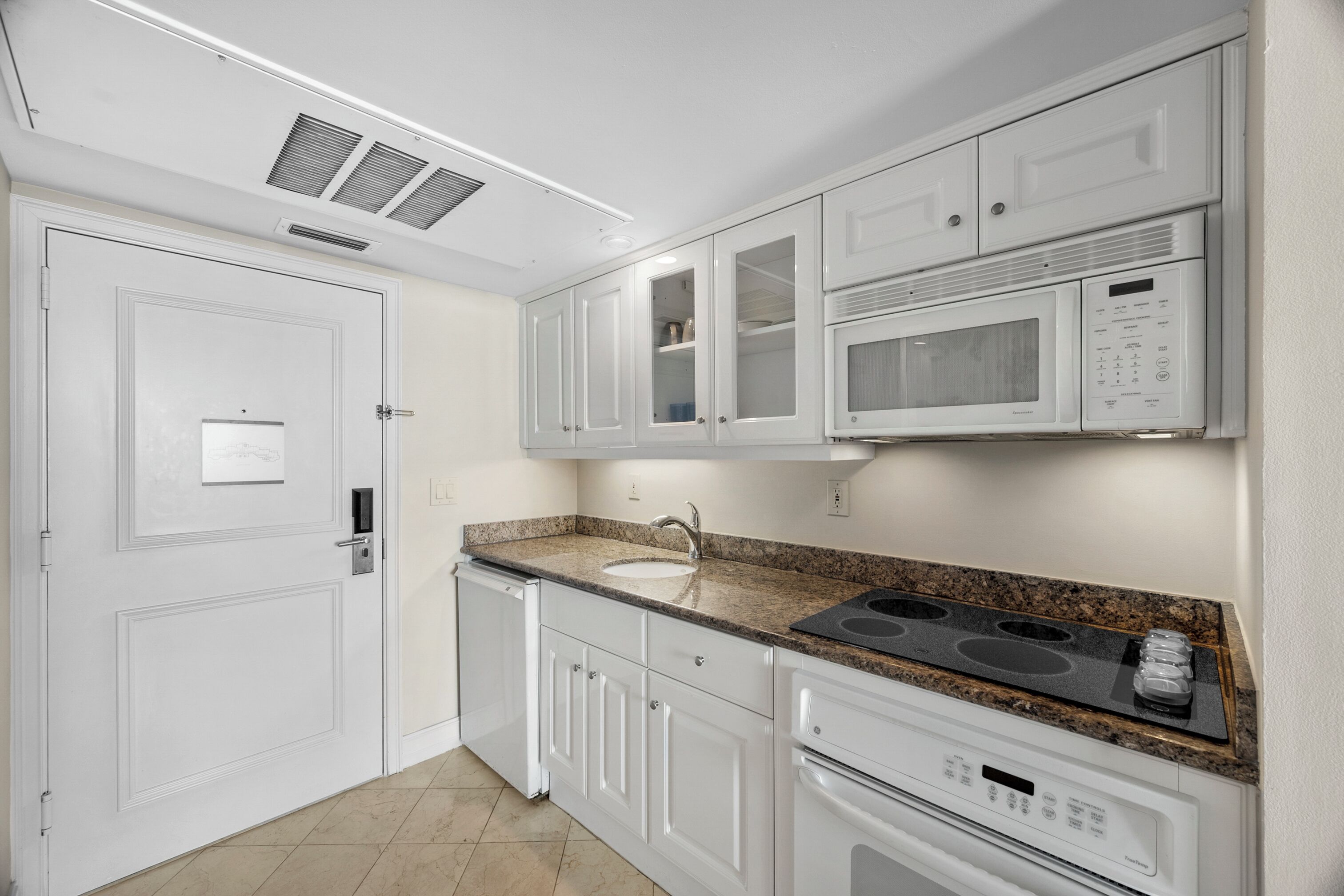 A modern kitchen with white cabinetry, a granite countertop, a built-in microwave, and a stainless steel range hood.