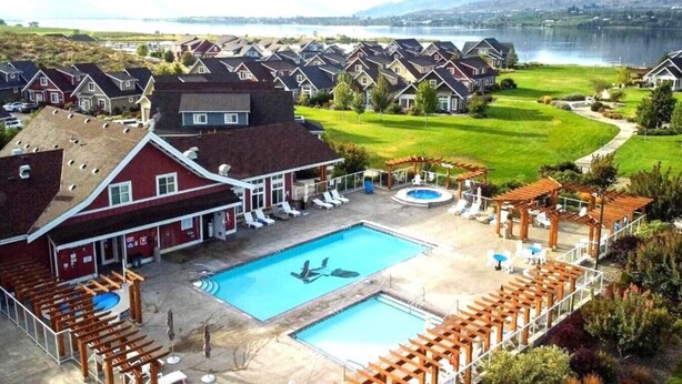 Un quartier résidentiel doté d’une piscine, de chaises longues et offrant une vue sur un lac et des montagnes.