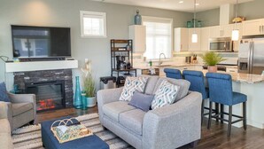 Un salon moderne avec un canapé, un pouf et un téléviseur à écran plat.