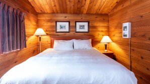 A wooden-paneled room with a bed, two bedside lamps, and two framed pictures on the wall.