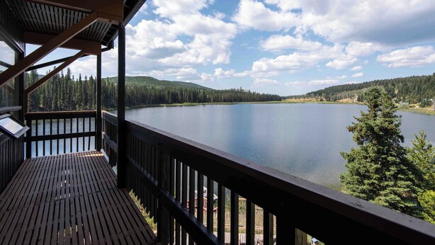 A wooden deck with a view of a calm lake, surrounded by forested hills.