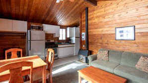A cozy cabin interior with wooden walls, a dining area with wooden furniture, a kitchenette, and a fireplace.