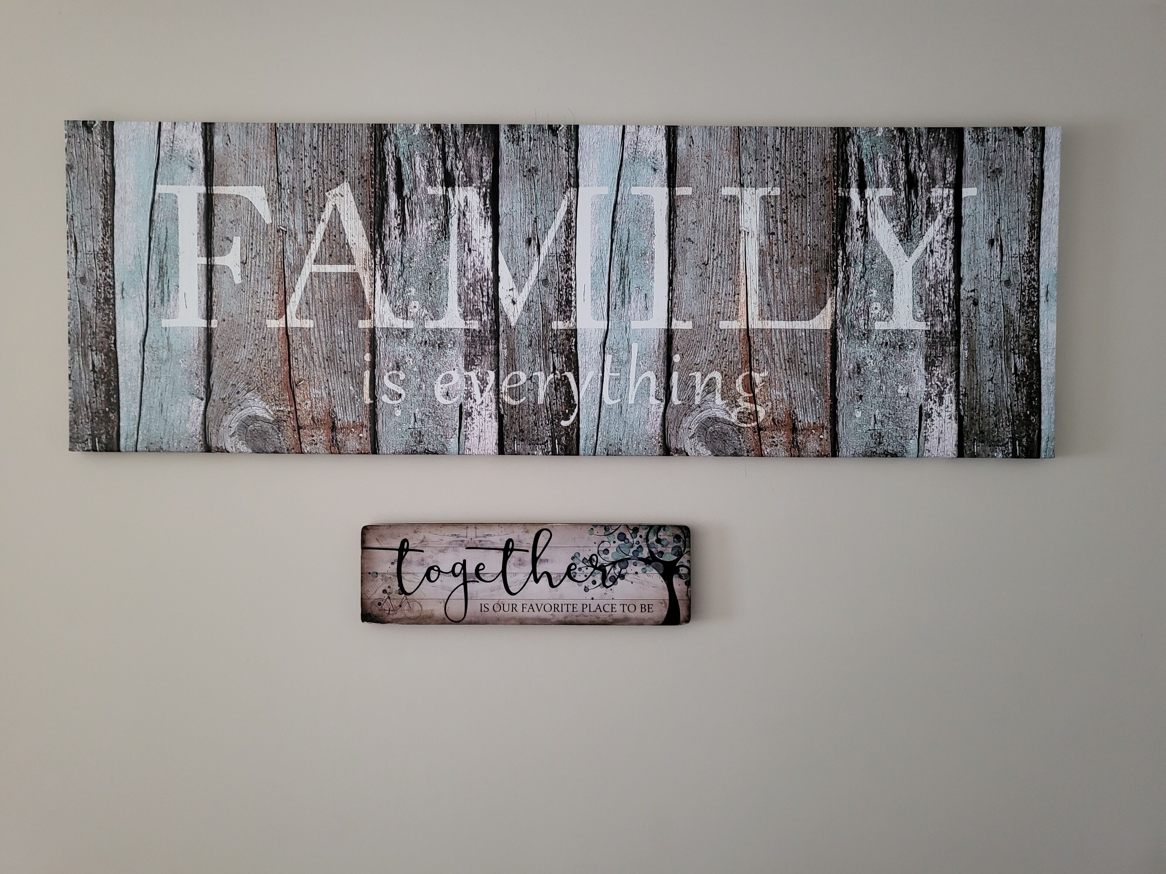 A wooden sign with the word "FAMILY" and the phrase "is everything" on a rustic background. Below it, a smaller sign reads "together is our favorite place to be."