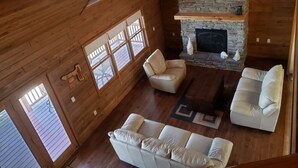 Amplia sala de estar con chimenea de piedra, paredes de madera y ventanas grandes.