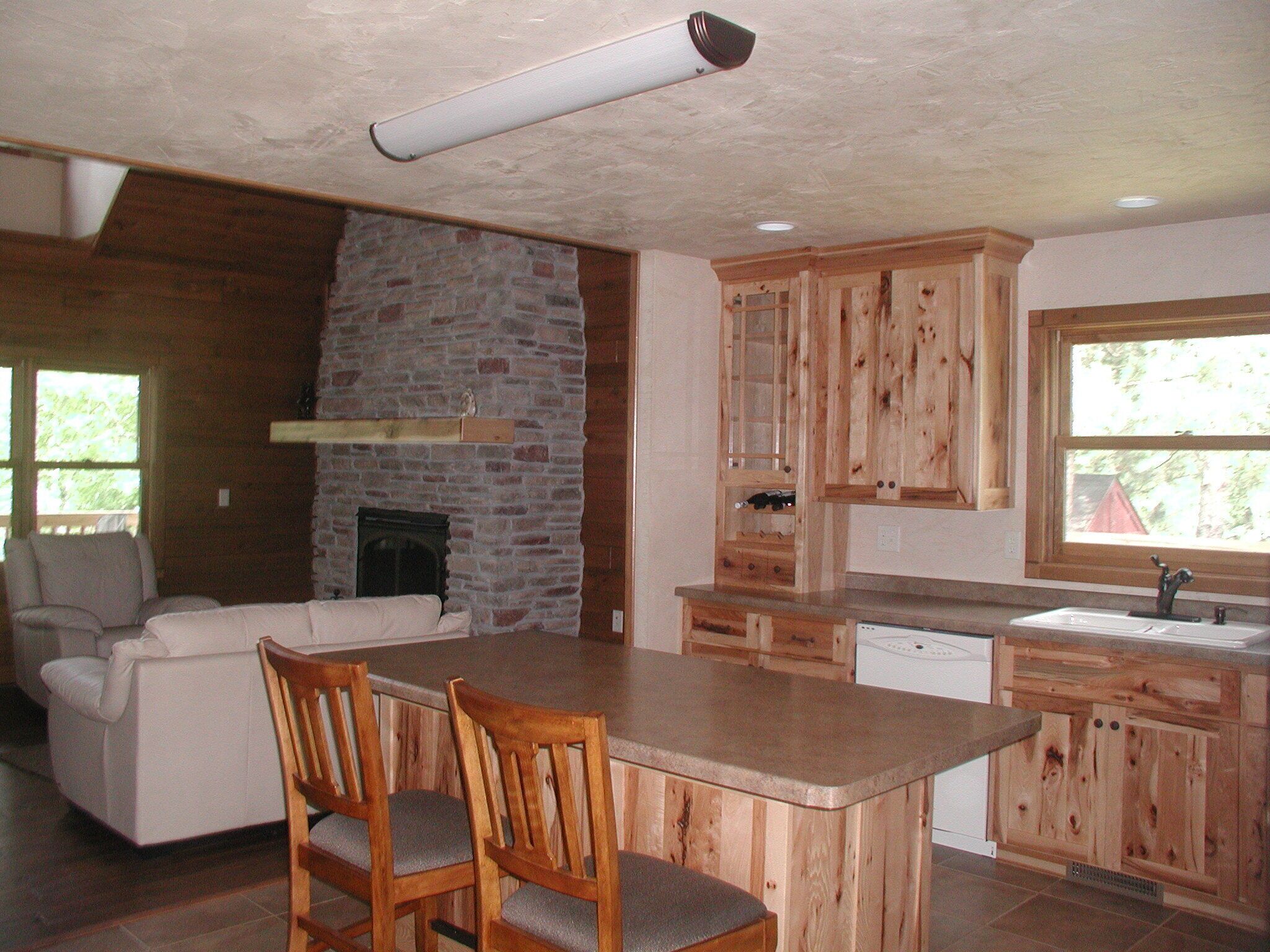 A spacious kitchen with wooden cabinets, a stone fireplace, and a large island with chairs.