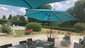 Un área de comedor al aire libre con una mesa dispuesta para cuatro personas, rodeada de sillas y cubierta por una sombrilla grande.