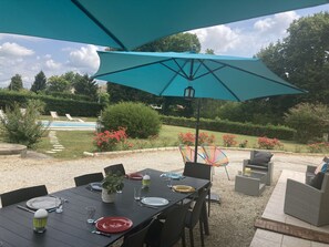Ein Essbereich im Freien mit einem Tisch für vier Personen, umgeben von Stühlen, unter einem großen Sonnenschirm.