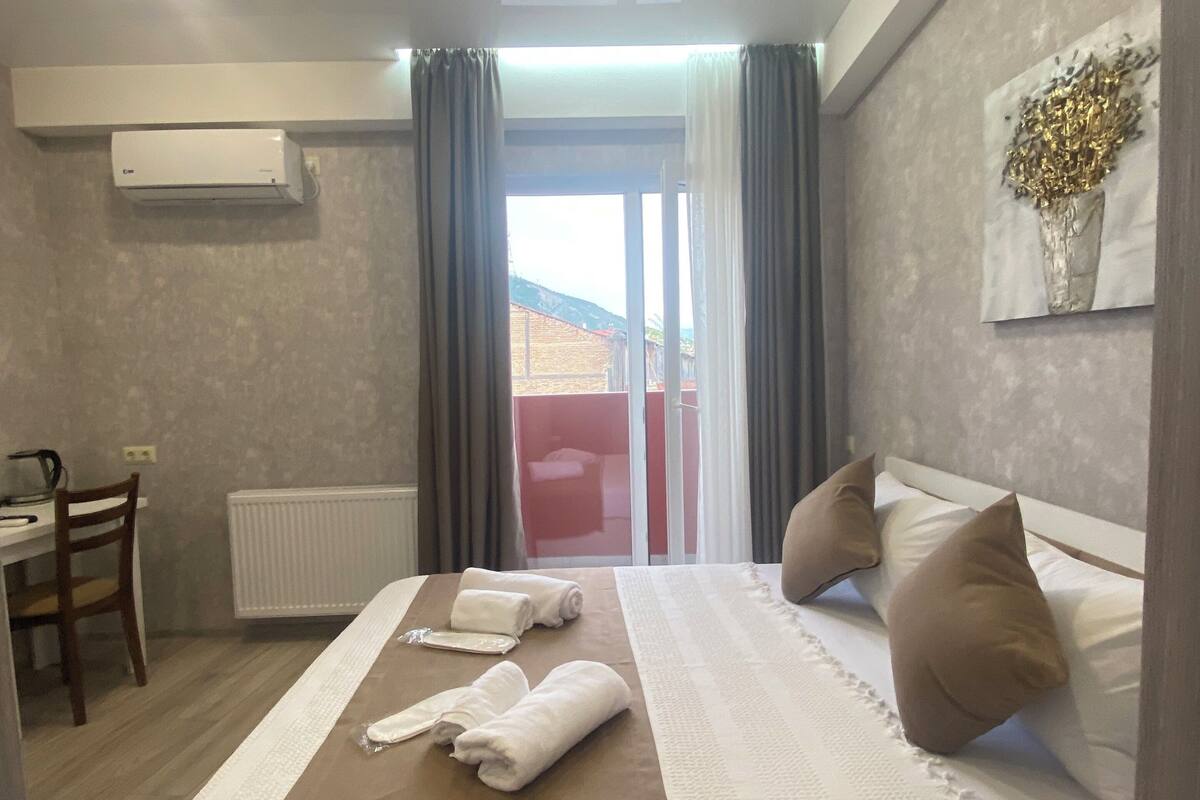 A hotel room with a bed, a desk, and a view of the outside.