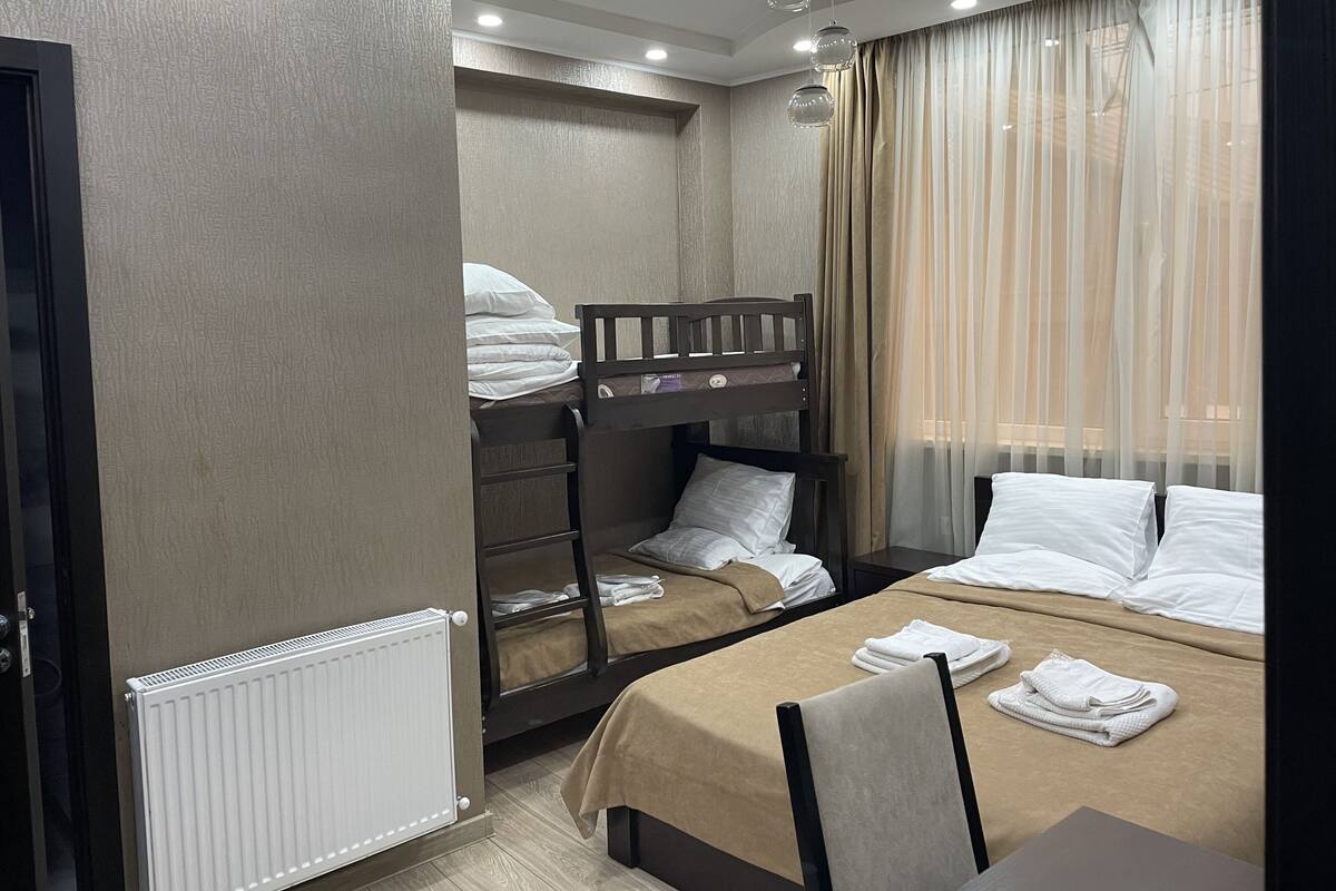 A hotel room with bunk beds, a radiator, a table with towels, and a window with curtains.
