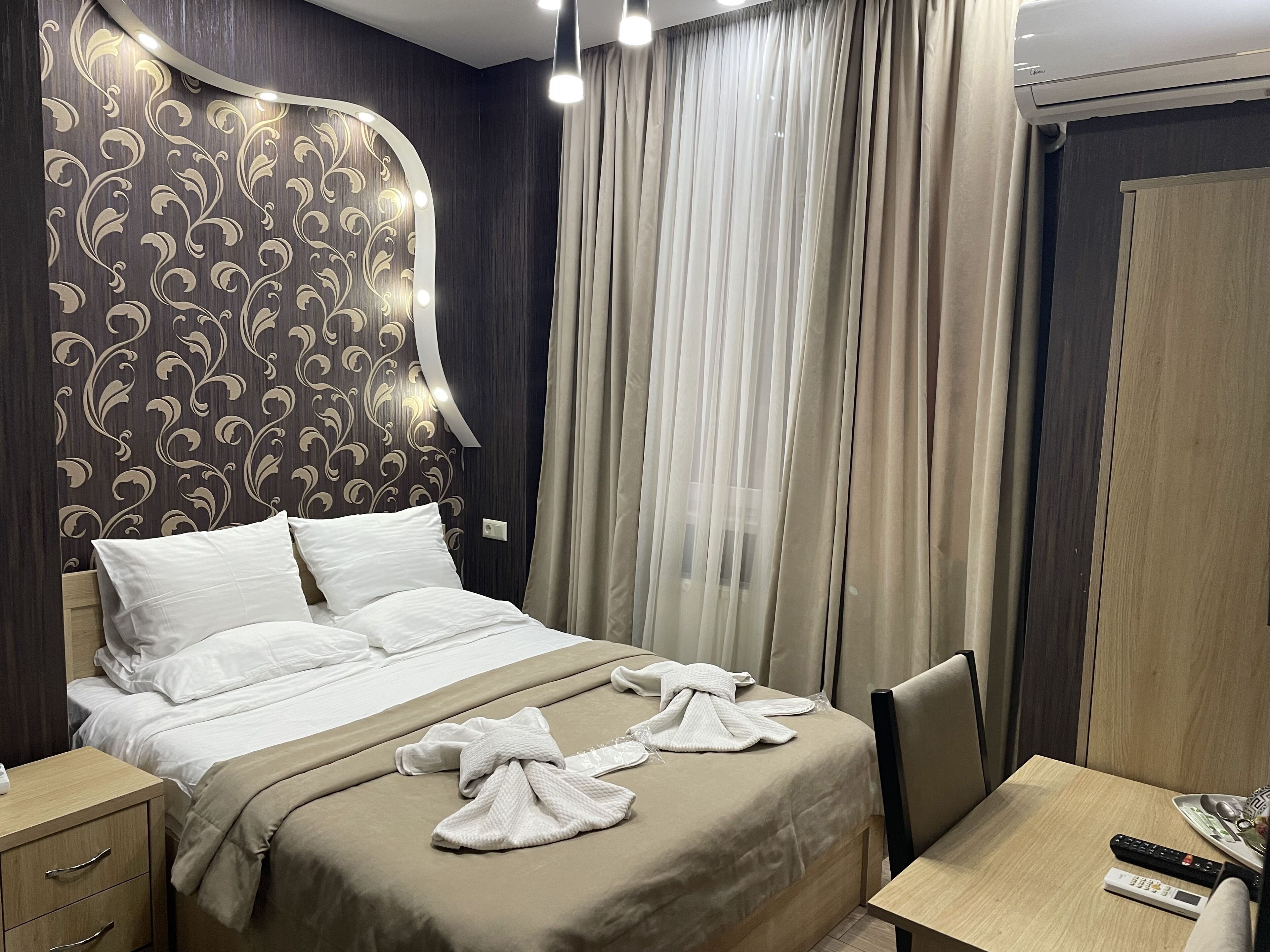 A hotel room with a large bed, a bedside table, a chair, a desk, and a wardrobe.