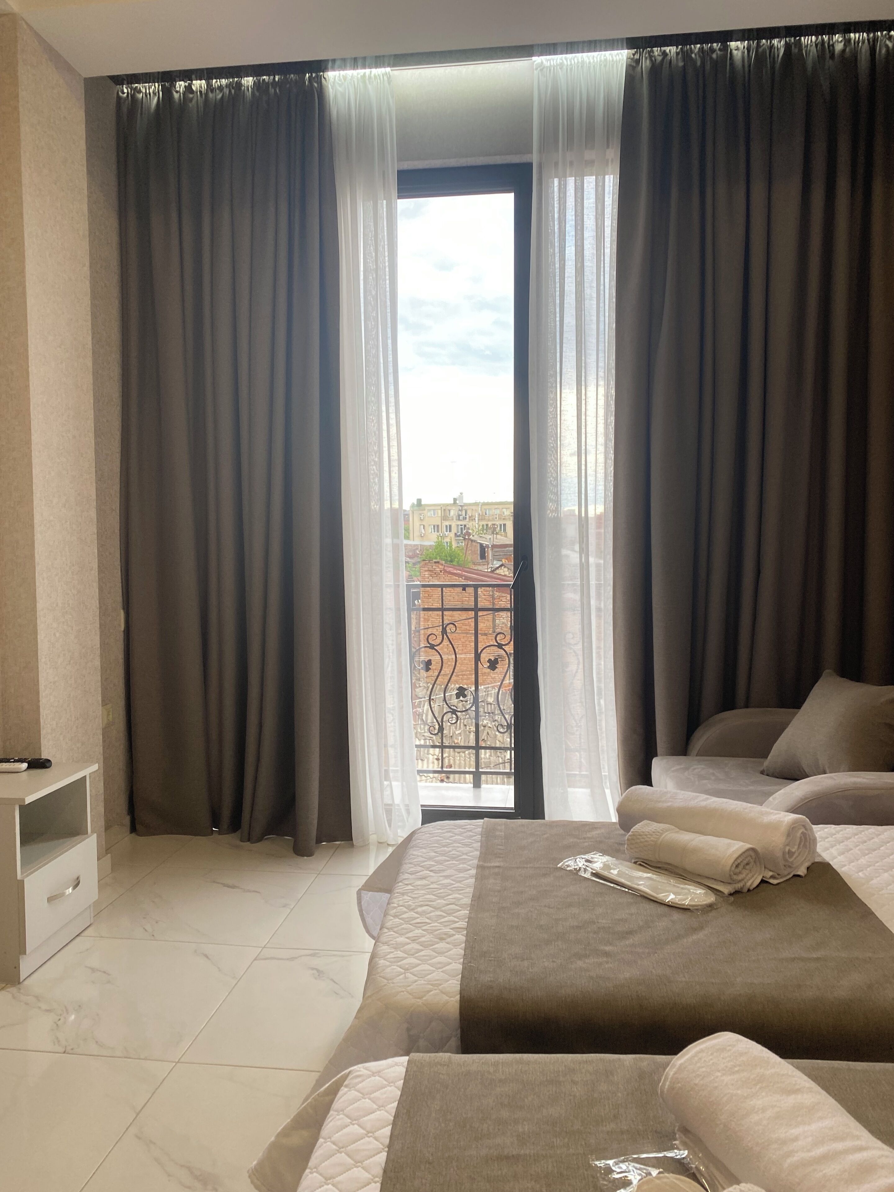 Hotellihuone, jossa on sänky, pieni yöpöytä ja parvekkeelta avautuva näkymä kaupunkiin.
