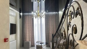 Un salón moderno con una araña, una mesa redonda y una escalera con barandillas metálicas ornamentadas.