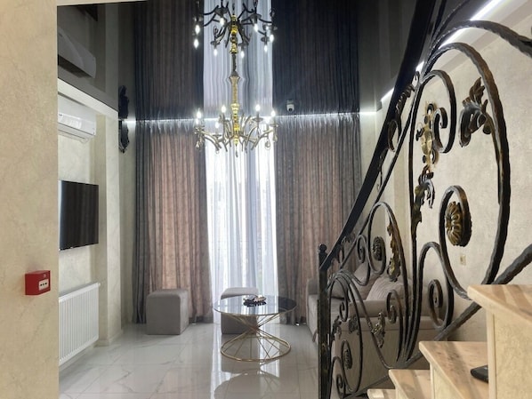 A modern living room with a chandelier, a round table, and a staircase with ornate metal railings. - Mimino T&G (Tbilisi)