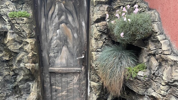 A stone wall with a rustic wooden door and a small garden area with plants and flowers. - Mimino T&G (Tbilisi)