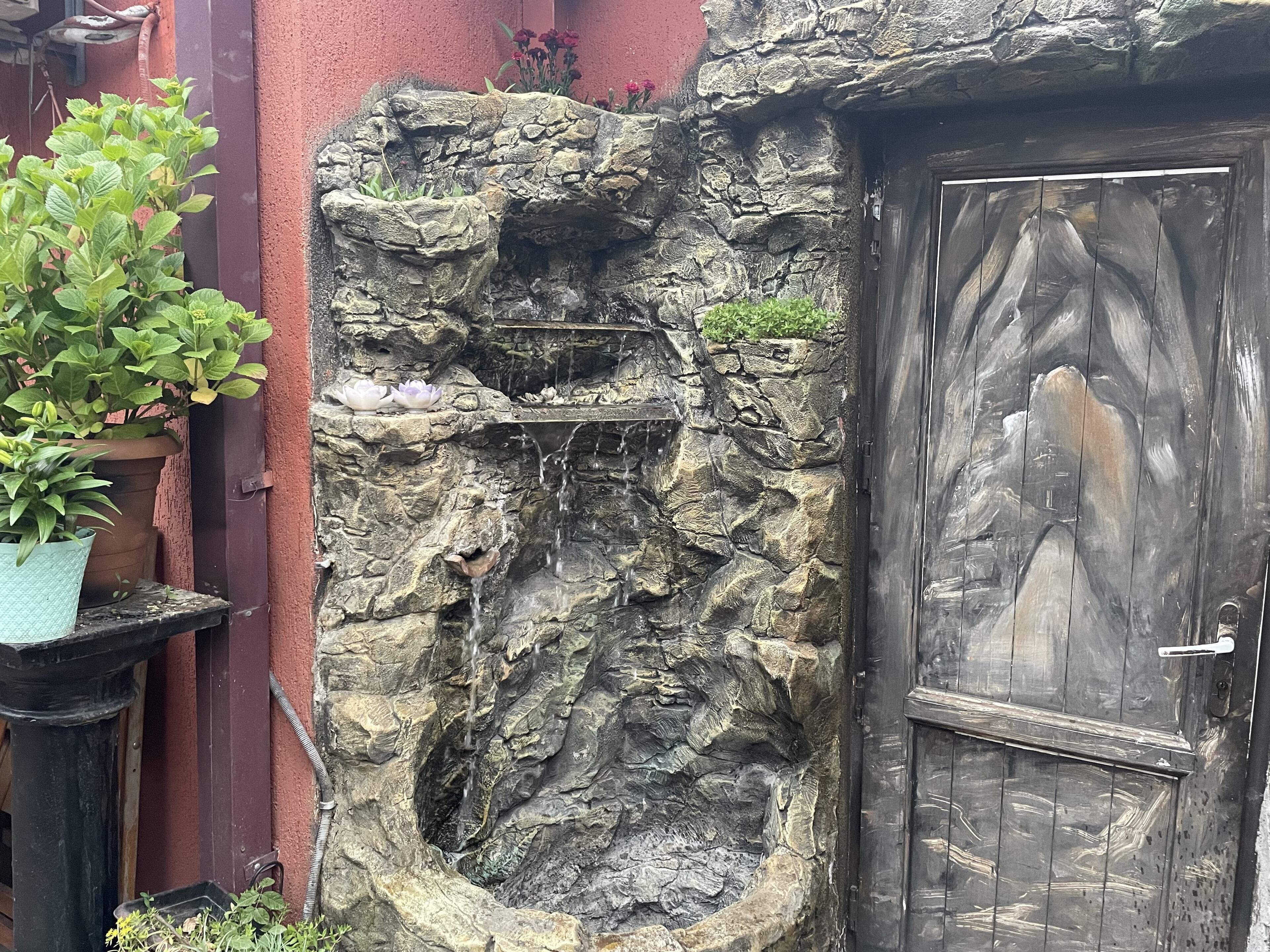 Eine rustikale Steinmauer mit einem kleinen Wasserfall und einer Holztür.
