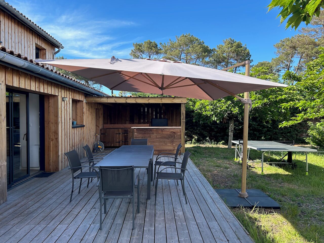 A wooden deck with a table and chairs, an umbrella, and a grill area.